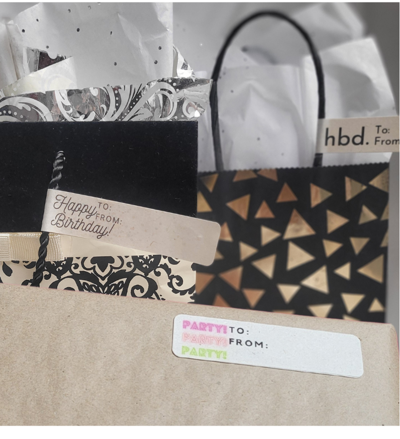 Gift bags with birthday Boy and Birthday Girl greeting labels. One wrapped present with a label with Birthday written 3 times