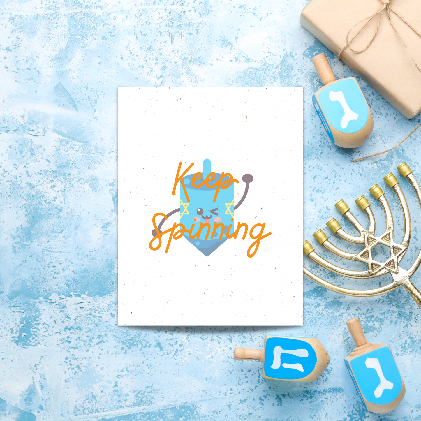 Card with 'Keep Spinning' text  over a personified dreidel surrounded by Hanukkah-themed items on a blue textured background