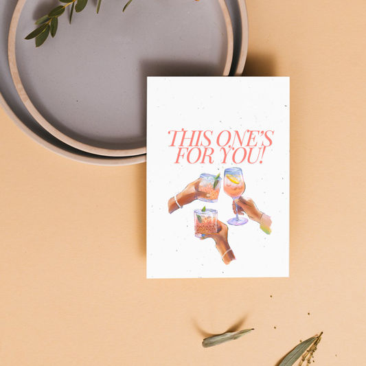 Greeting card with 'This one's for you!' text and illustrations of female hands holding drinks on a beige background.