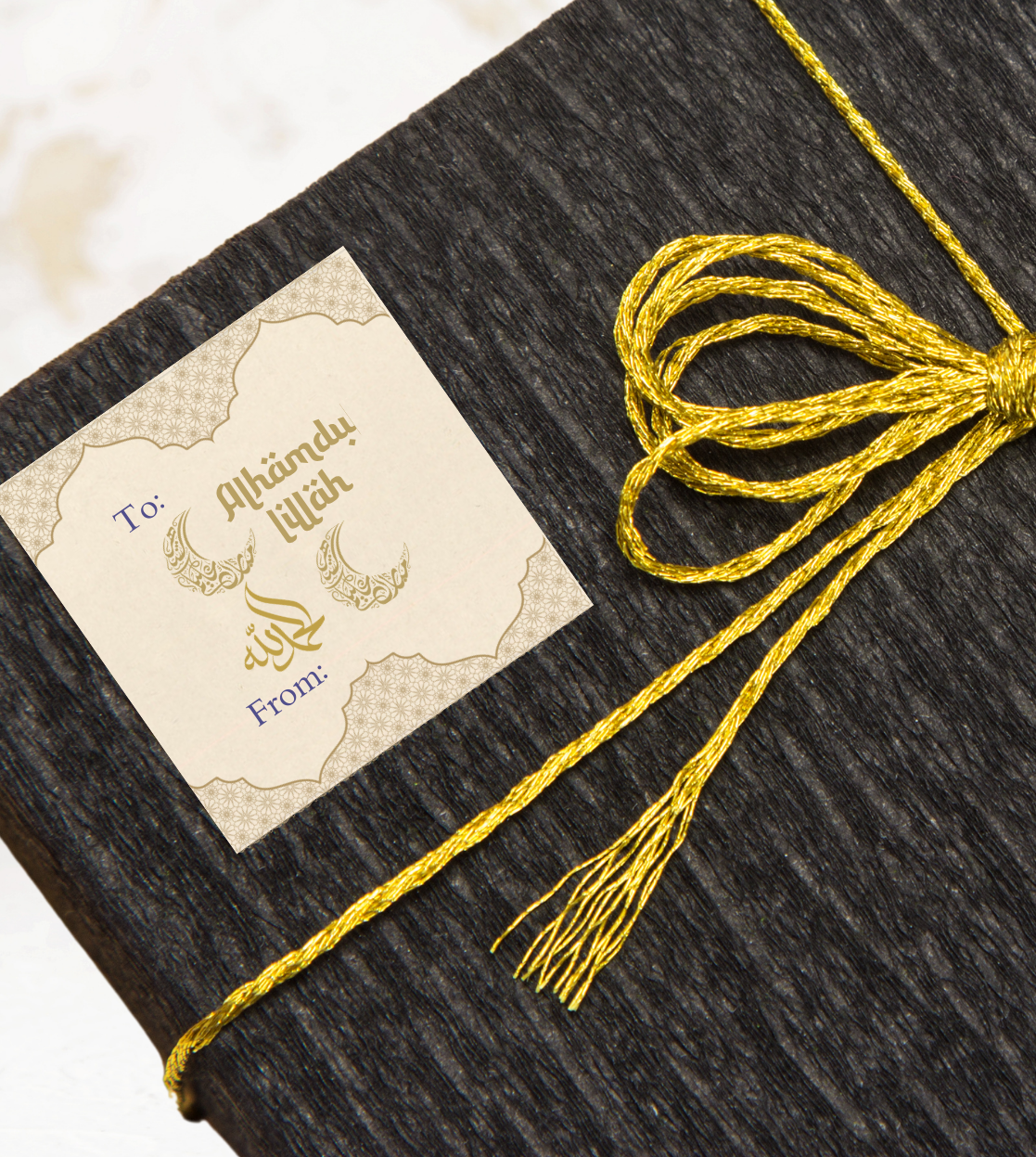 Dark textured gift box with a gold ribbon and a gift sticker label with 'Alhamdulillah' text on a light background