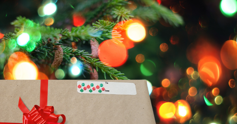 A wrapped present with a greeting label on it. The greeting label has Christmas ball ornaments hanging.