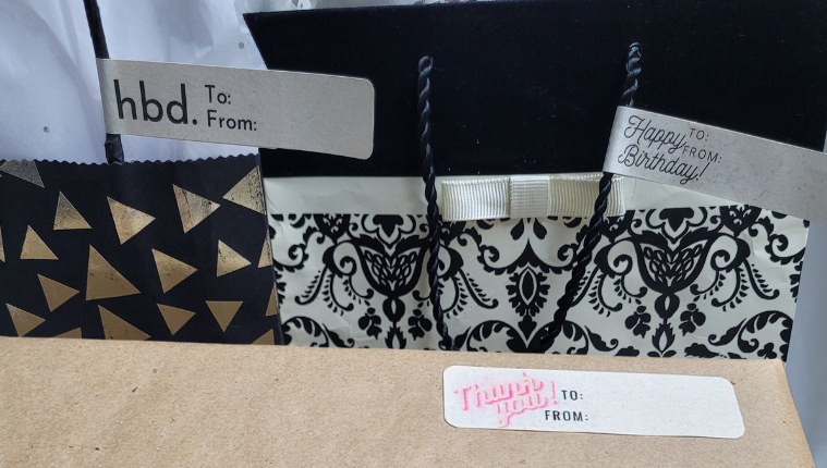 Two gift bags. One with a greeting label written "HBD" in bold aerial font. One with a greeting label written "Happy Birthday" in Italics. One wrapped present with craft paper and a greeting label written "Thank you" in red and white retro font