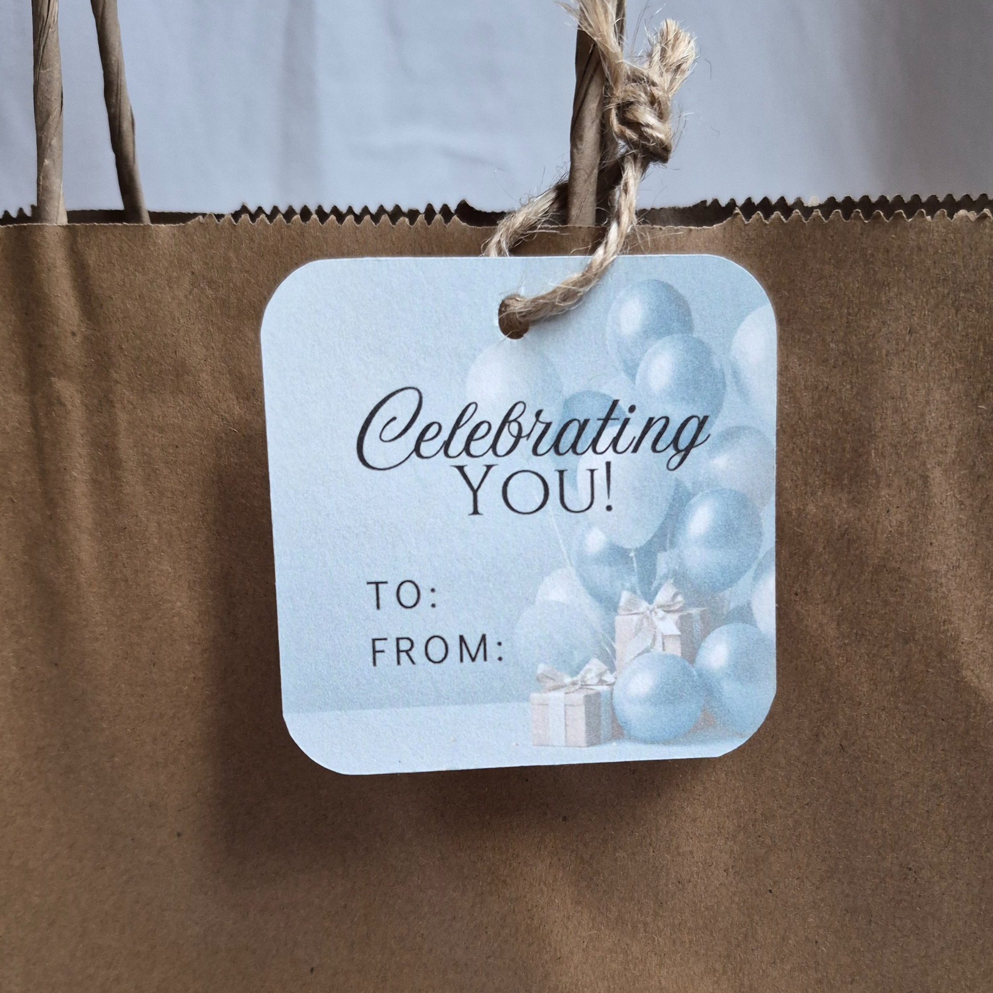 Gift tag with 'Celebrating You!' text and balloons on a brown paper bag.