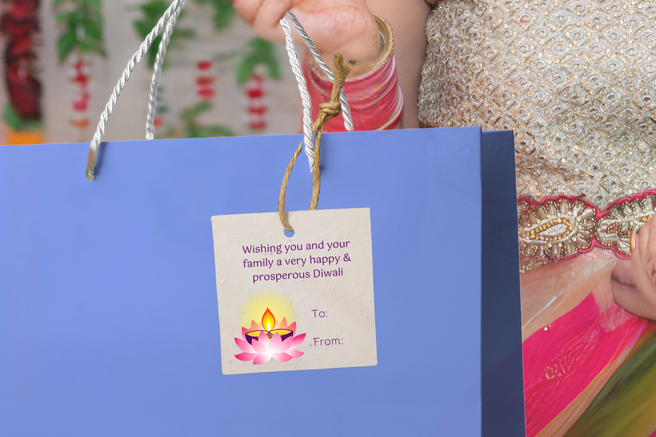Woman holding a blue gift bag with a that has a gift tag with a Diwali message against a colorful background