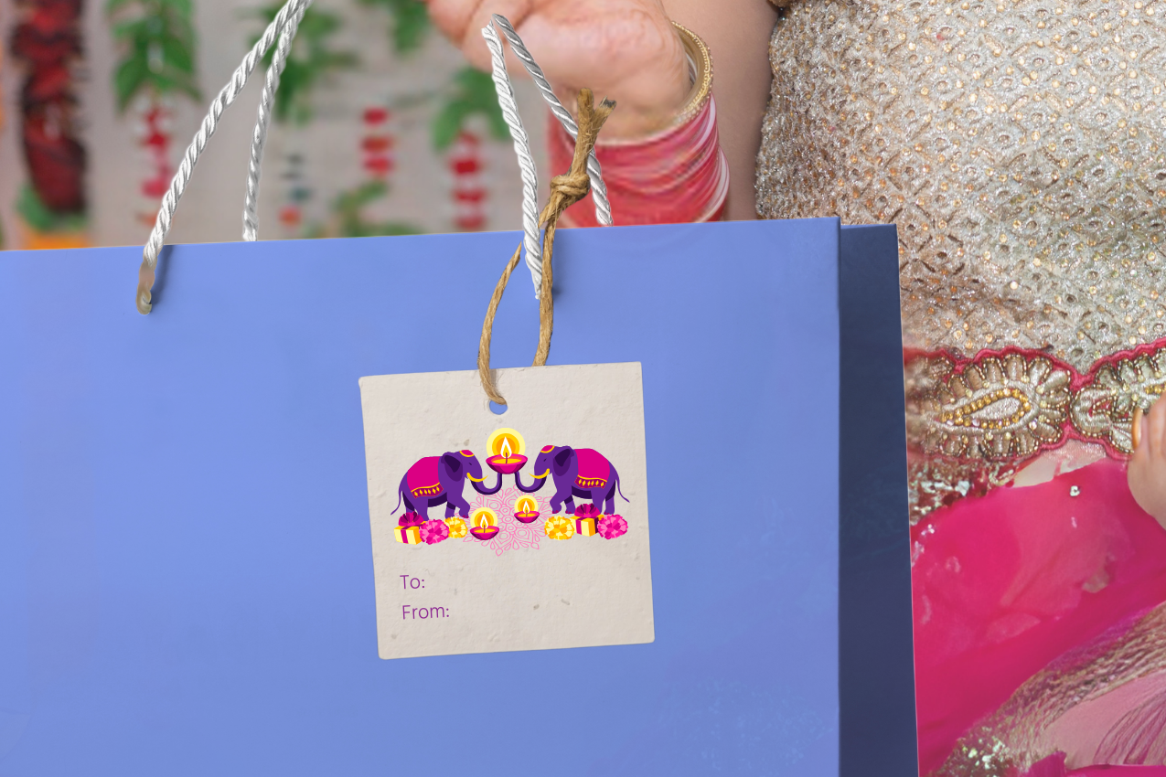 Woman in traditional attire holding a blue gift bag with a decorative tag with elephants for Diwali against a colorful background