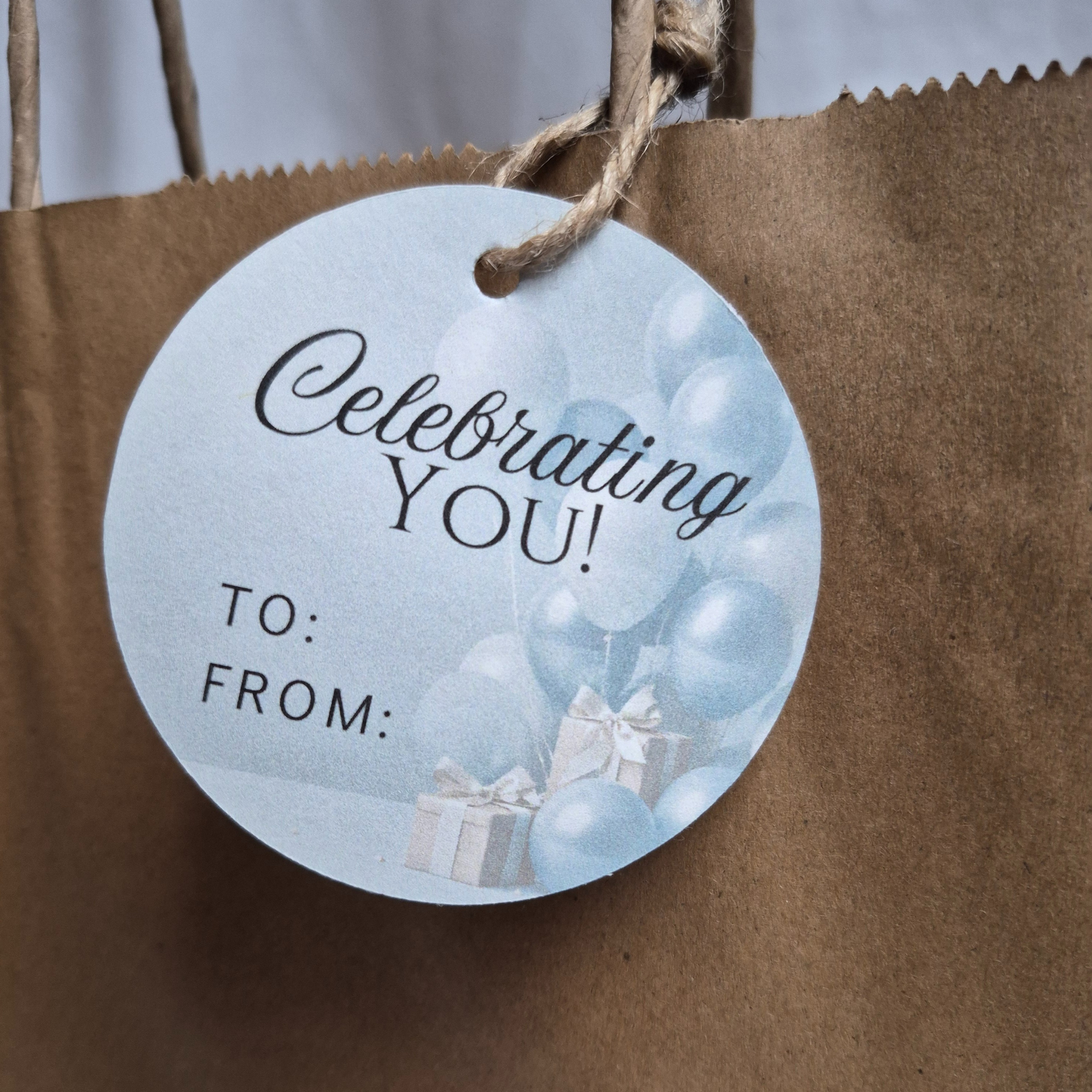 Round gift tag with 'Celebrating YOU!' text on a brown paper bag.