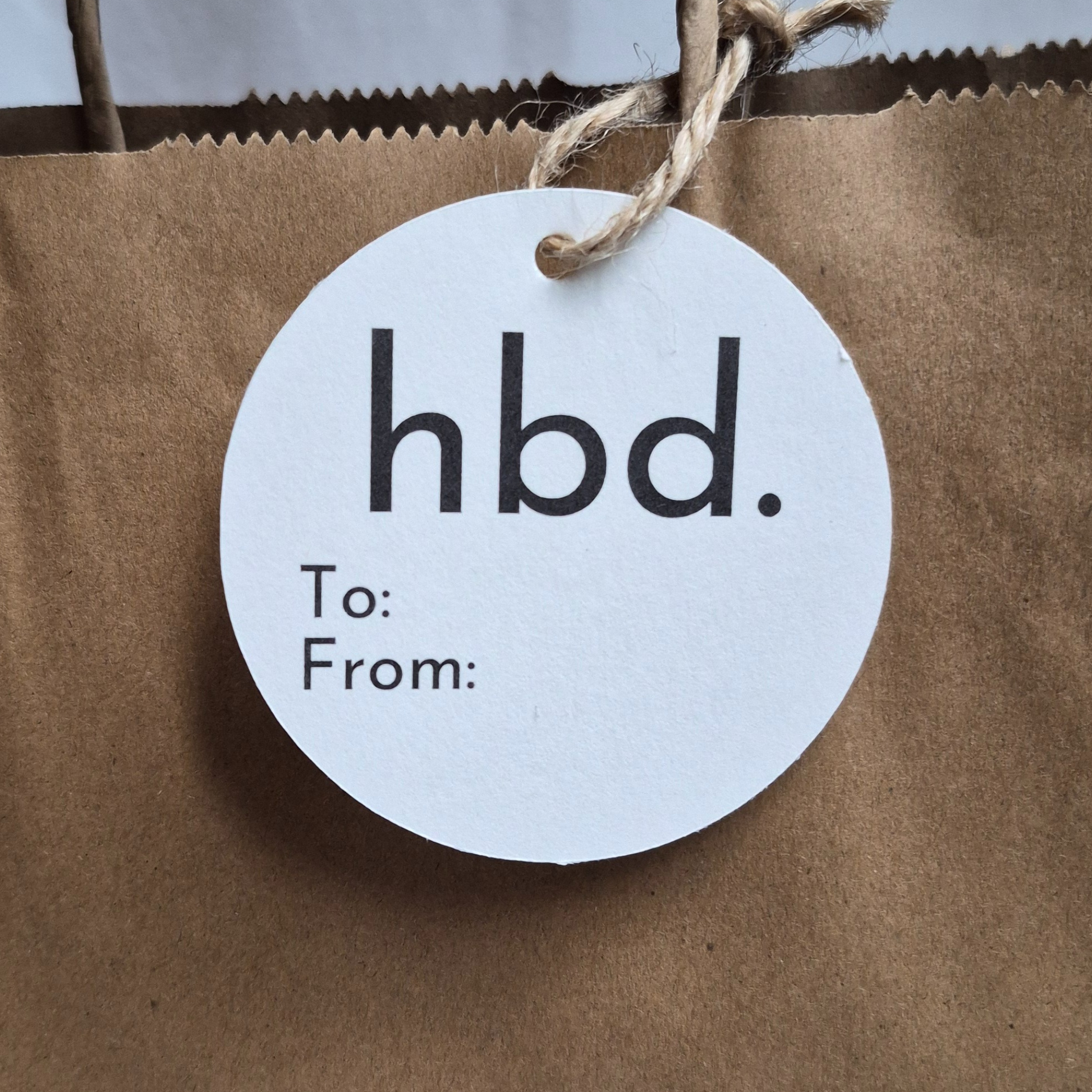 Round white tag with 'hbd.' text on a brown paper bag