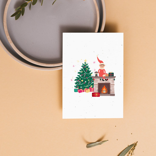 Christmas-themed greeting card with an elf by a fireplace and tree 