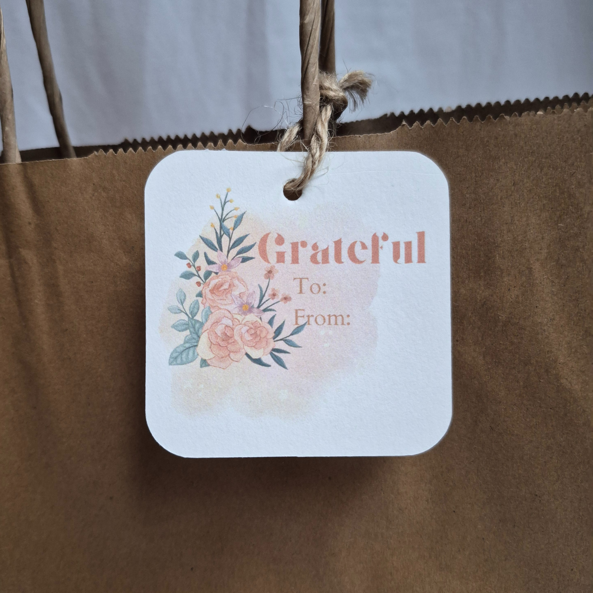 Gift tag with floral design and 'Grateful' text hanging on a brown paper bag.