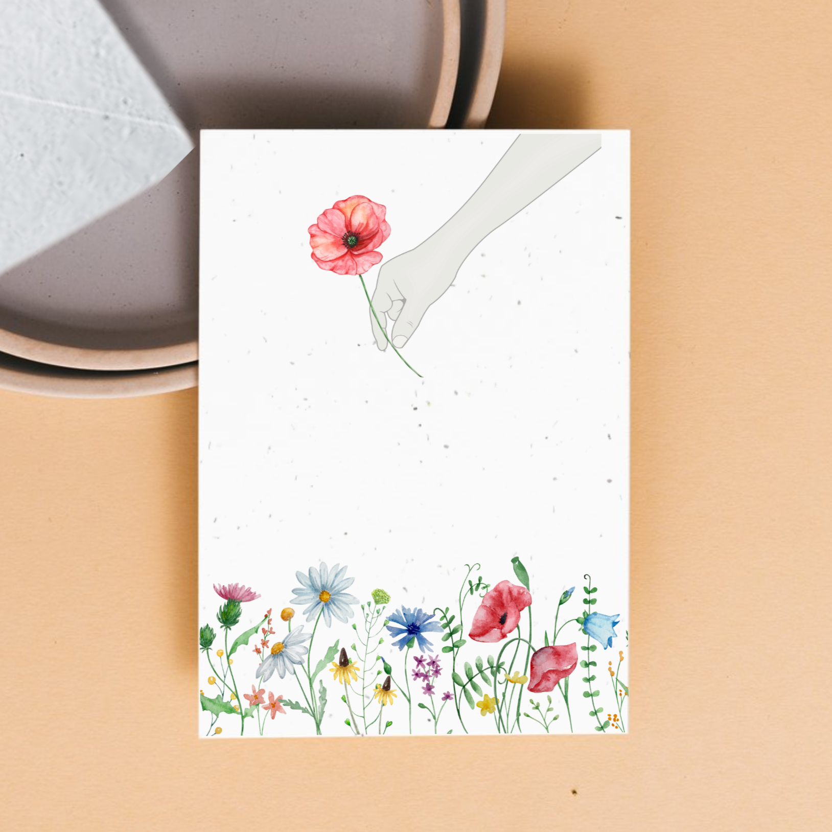 front of card with a garden of watercolour wildflowers and a hand picking one flower