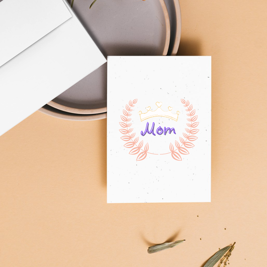 Mother's day greeting card with 'Mom' and a crown above 'Mom' surrounded by a floral design on a beige surface