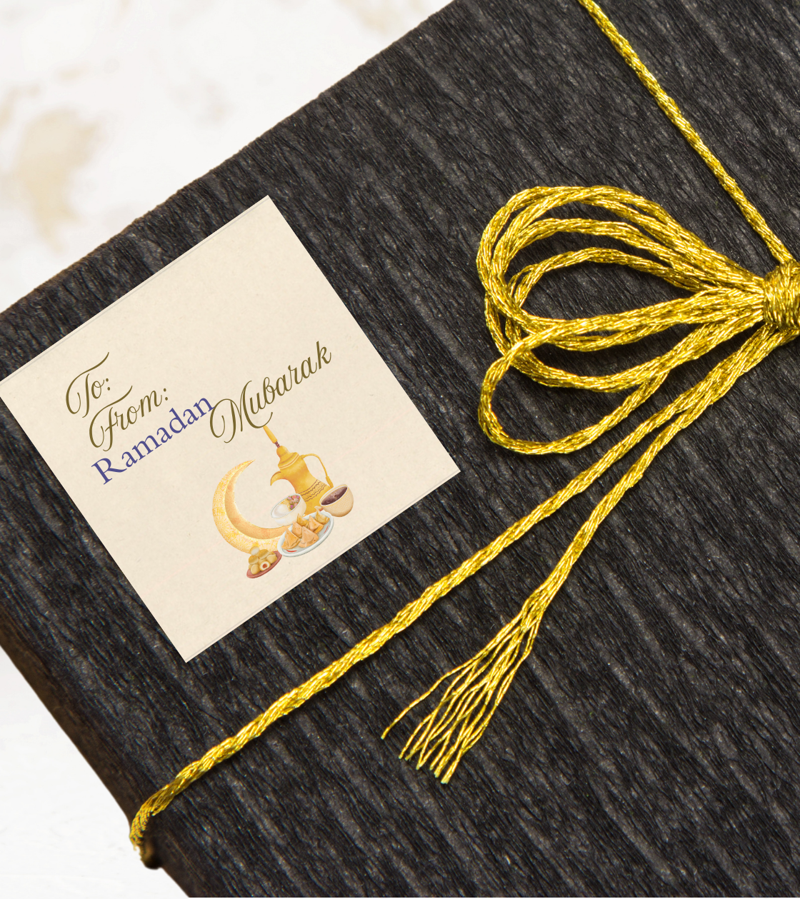 Black gift box with a gold ribbon and a gift sticker label with decorative 'Ramadan Mubarak' text