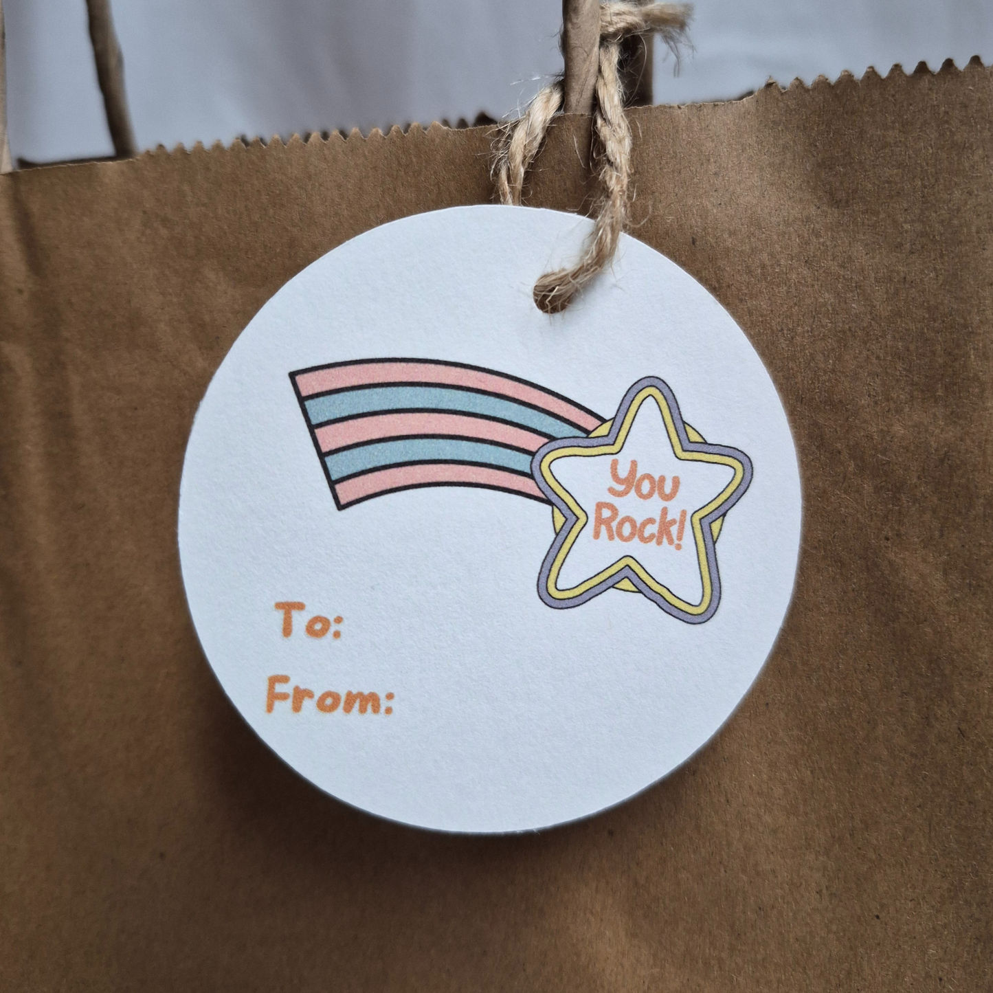Round congratulations gift tag made with recycled paper with rainbow and star with 'you rock' design on a brown paper bag