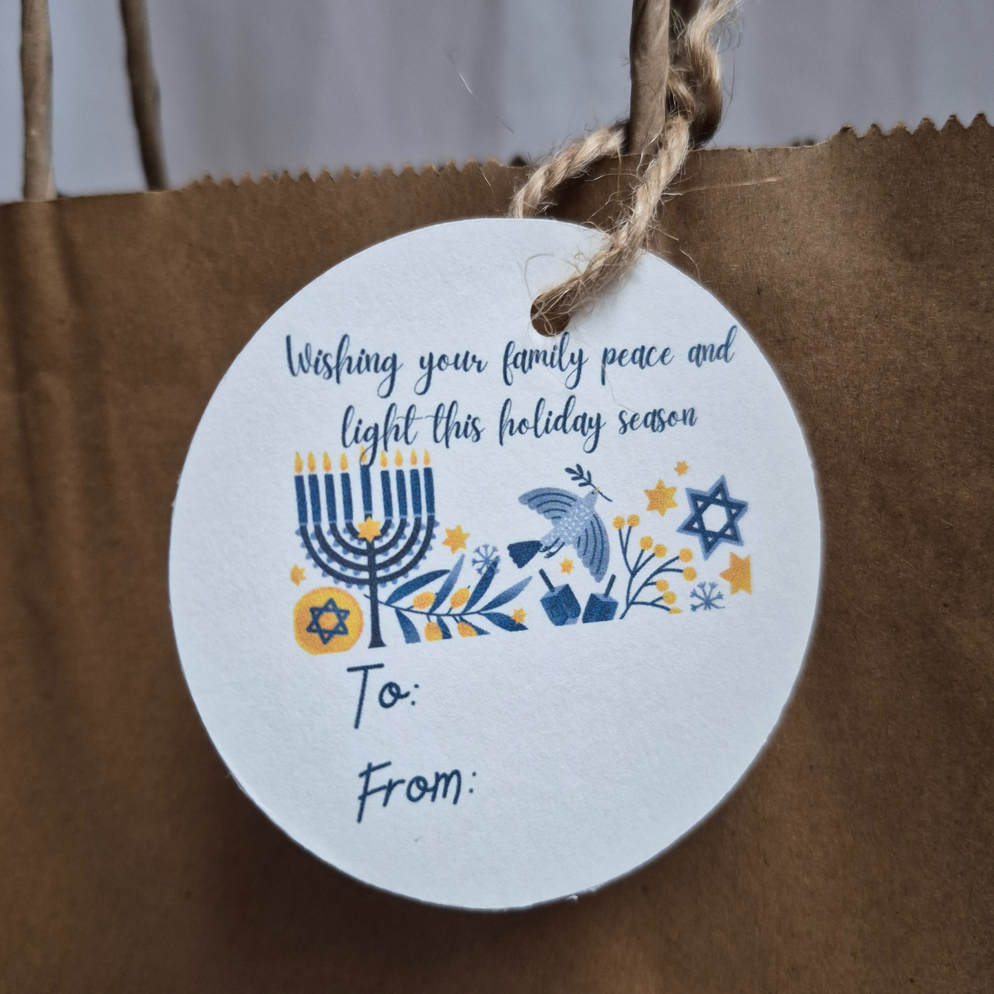 Round Hanukkah gift tag with 'wishing our family peace and light' text on a brown paper bag.