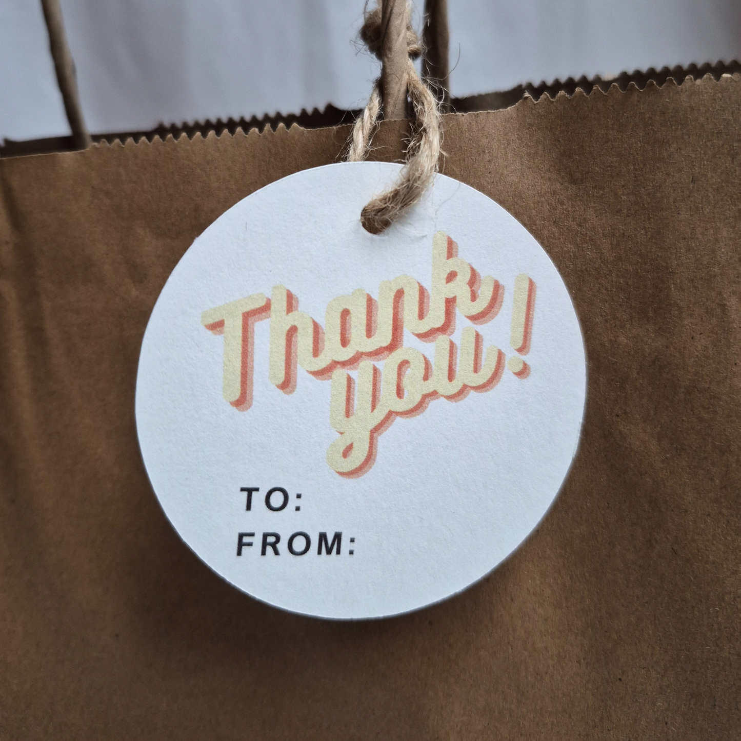 Round recycled paper gift tag with 'Thank you!' text in a retro design on a brown paper bag.