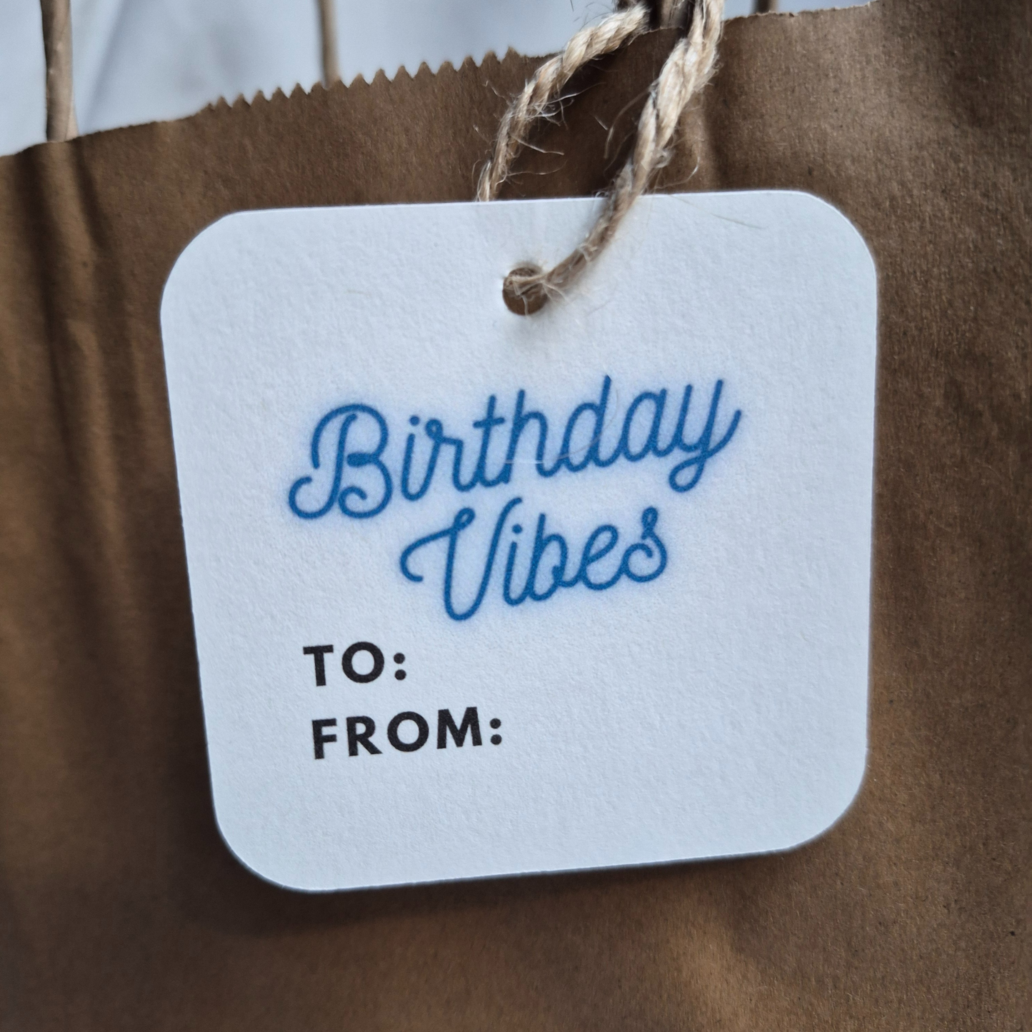 Square Birthday gift tag made of recycled paper with 'Birthday Vibes' text in neon blue on a brown paper bag