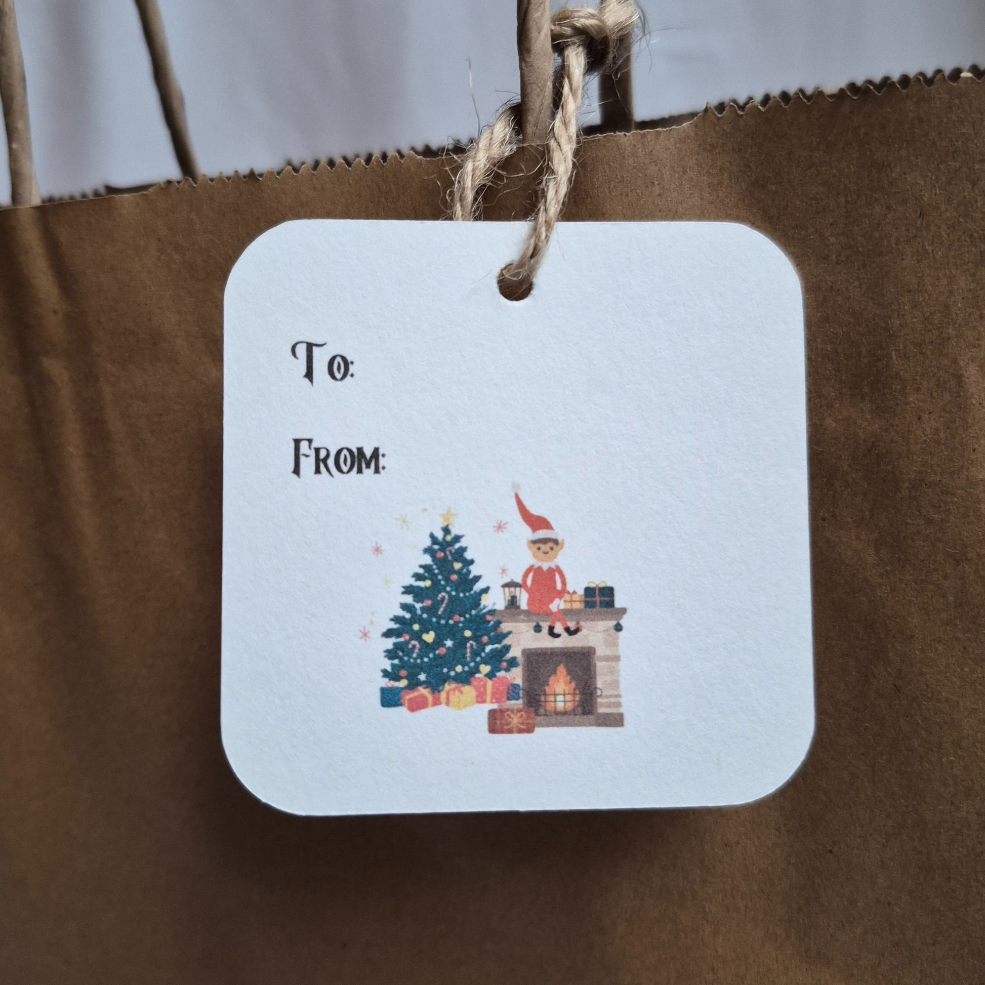 square recycled paper Gift tag with Christmas decor and elf on the shelf on a brown paper bag