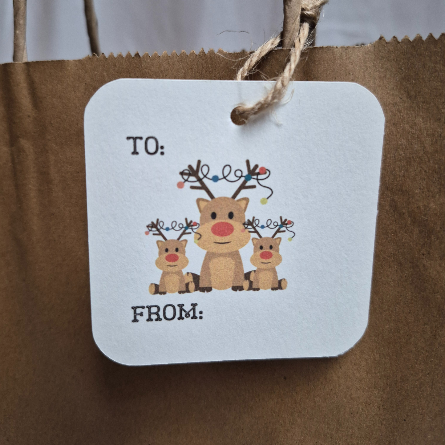 Square recycled paper Christmas gift tag with reindeer illustration on a brown paper bag