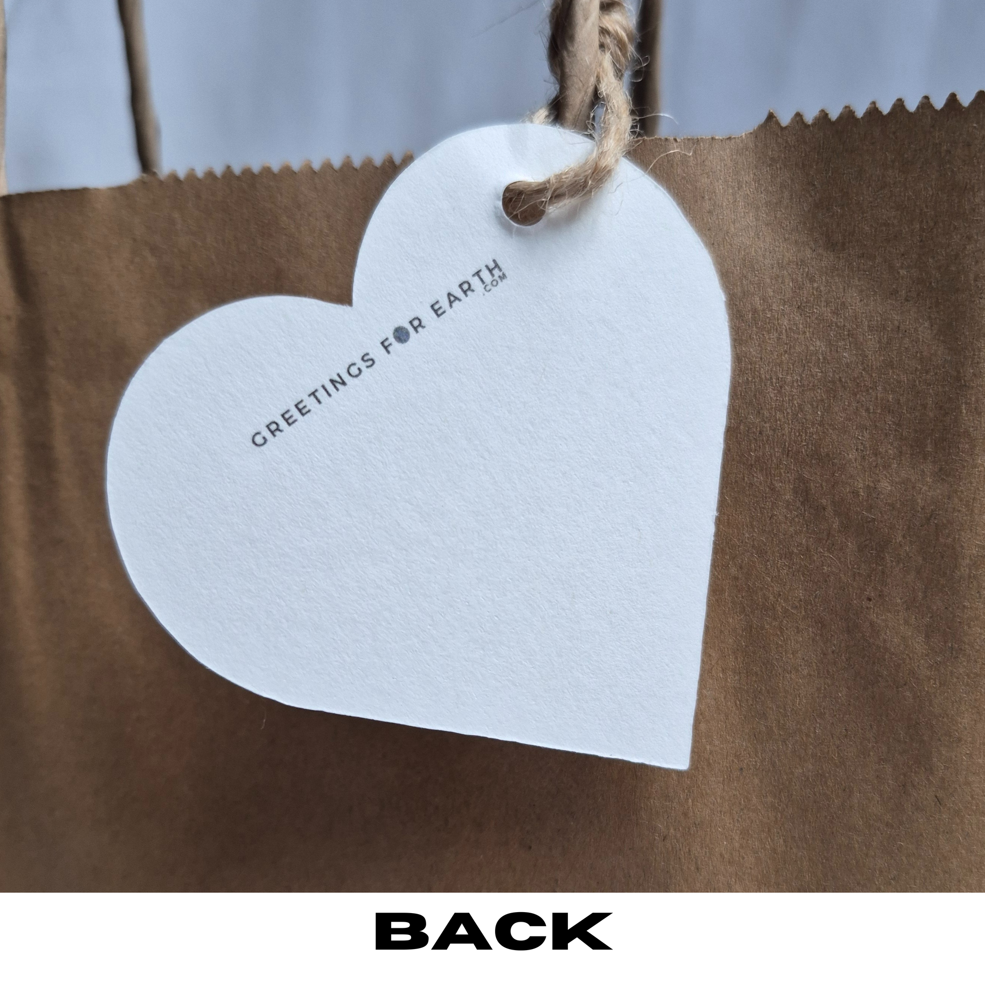 Back of Heart-shaped recycled paper tag with 'Greetings for Earth' text for website on a brown paper bag.