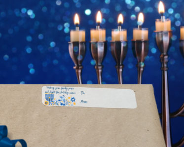 Wrapped gift with Menorah in the background the a gift label with: wishing your family peace and light this holiday season