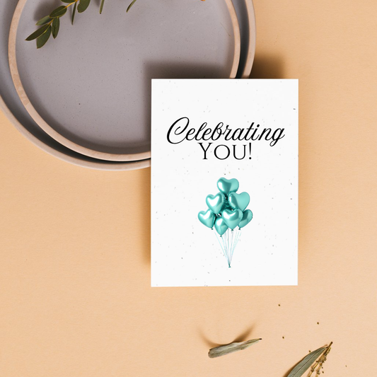 Celebratory seed paper greeting card with 'Celebrating YOU!' text and teal balloons on a beige background