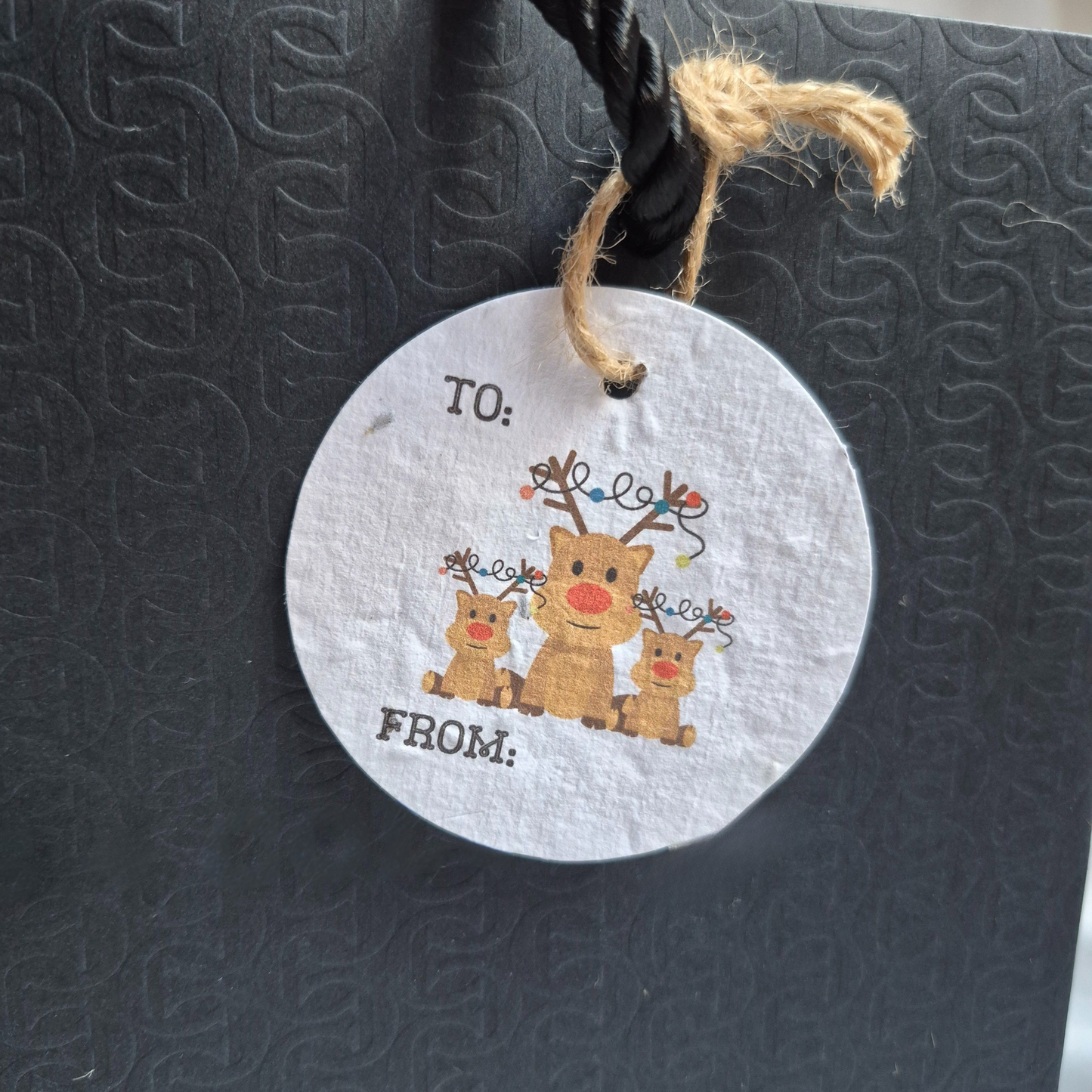 Round Christmas seed paper gift tag with reindeer illustration hanging from a black bag