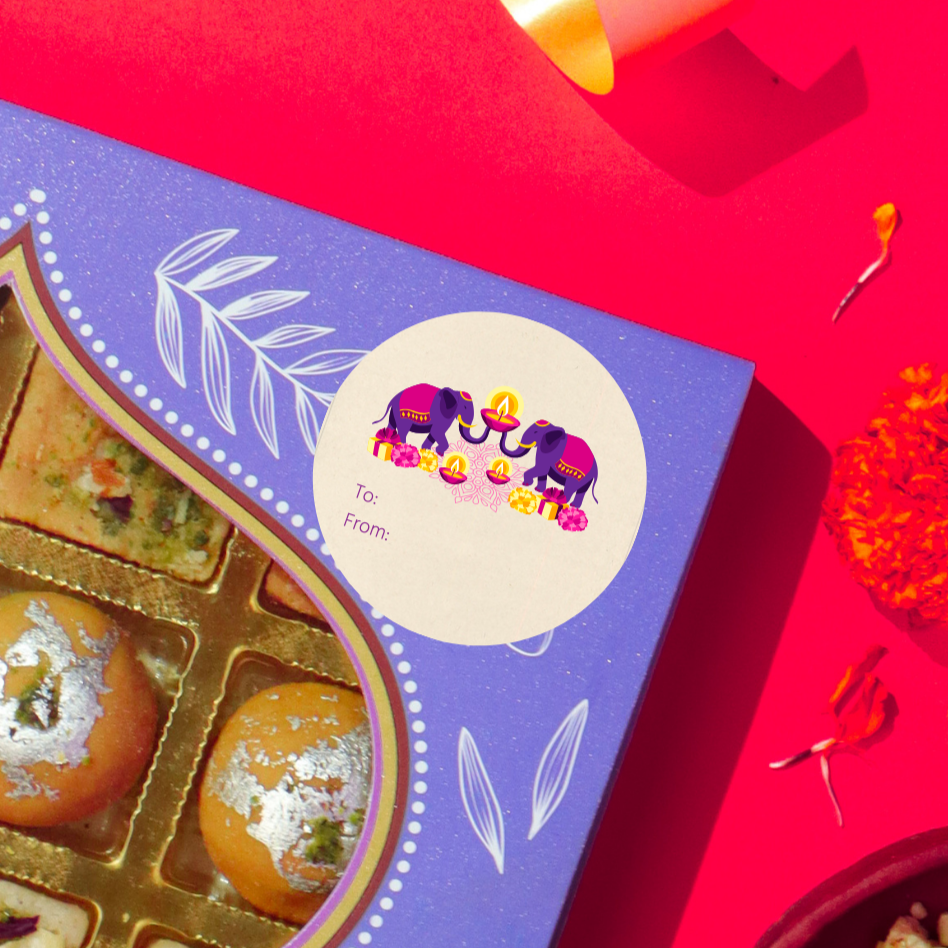 Diwali gift sticker, round, made from compostable sugarcane, with elephants and diyas illustration. The sticker label is placed on a gift box of Diwali sweets on a red background