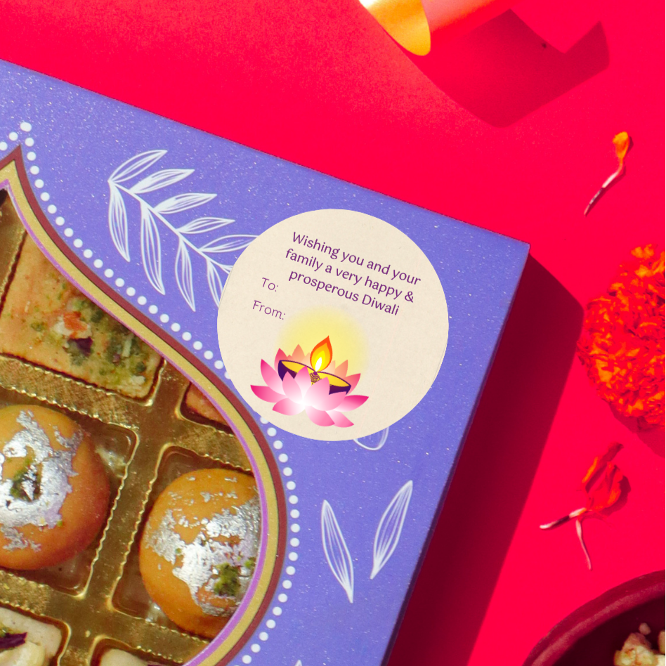 Diwali gift sticker, round, made from compostable sugarcane, with 'wishing you and your family a happy & prosperous Diwali' text and lotus illustration. The sticker label is placed on a gift box of Diwali sweets on a red background
