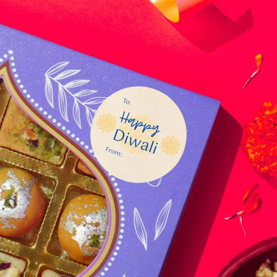 Diwali gift sticker, round, made from compostable sugarcane, with ''Happy Diwali' text and mandalas illustration. The sticker label is placed on a gift box of Diwali sweets on a red background