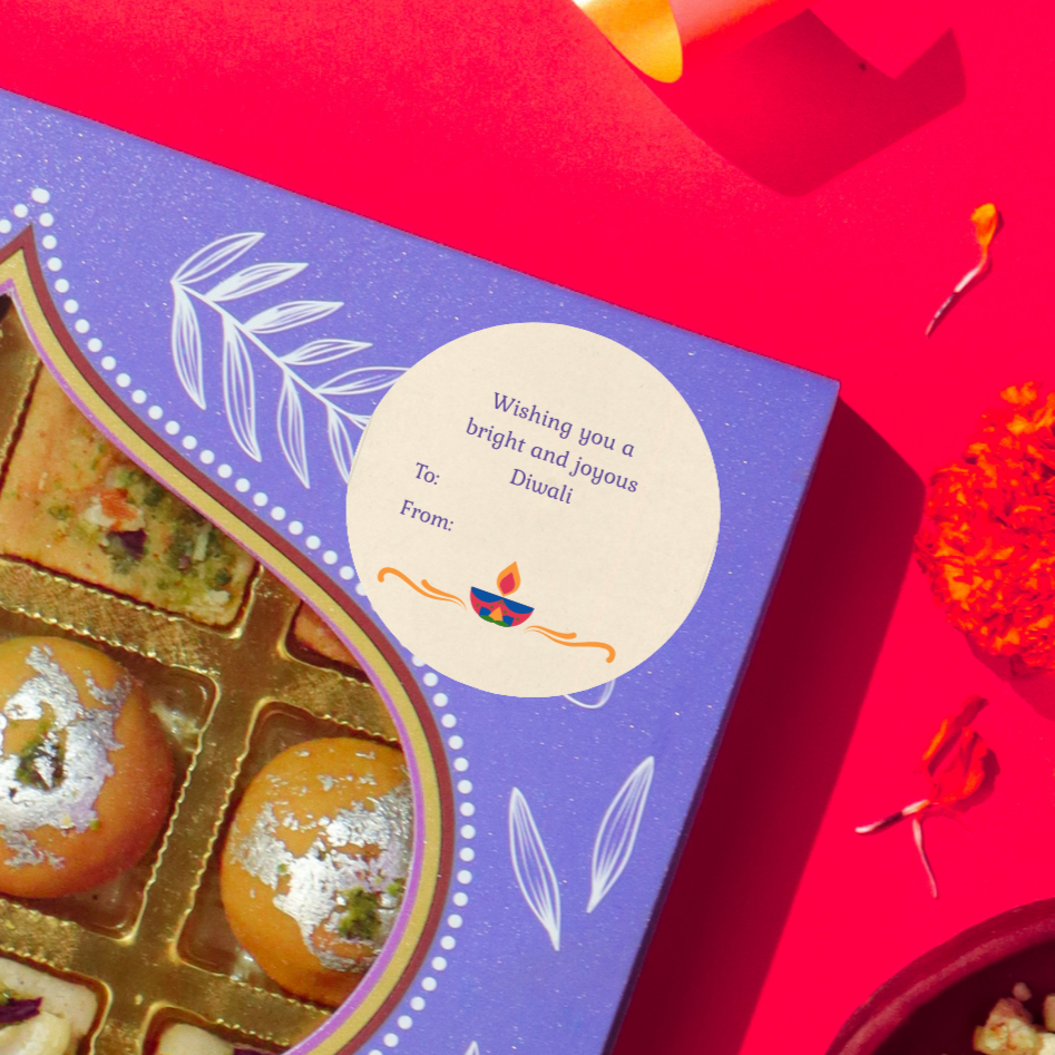 Diwali gift sticker, square, made from compostable sugarcane, with 'wishing you a bright joyous Diwali' text and Diya illustration. The sticker label is placed on a gift box of Diwali sweets on a red background