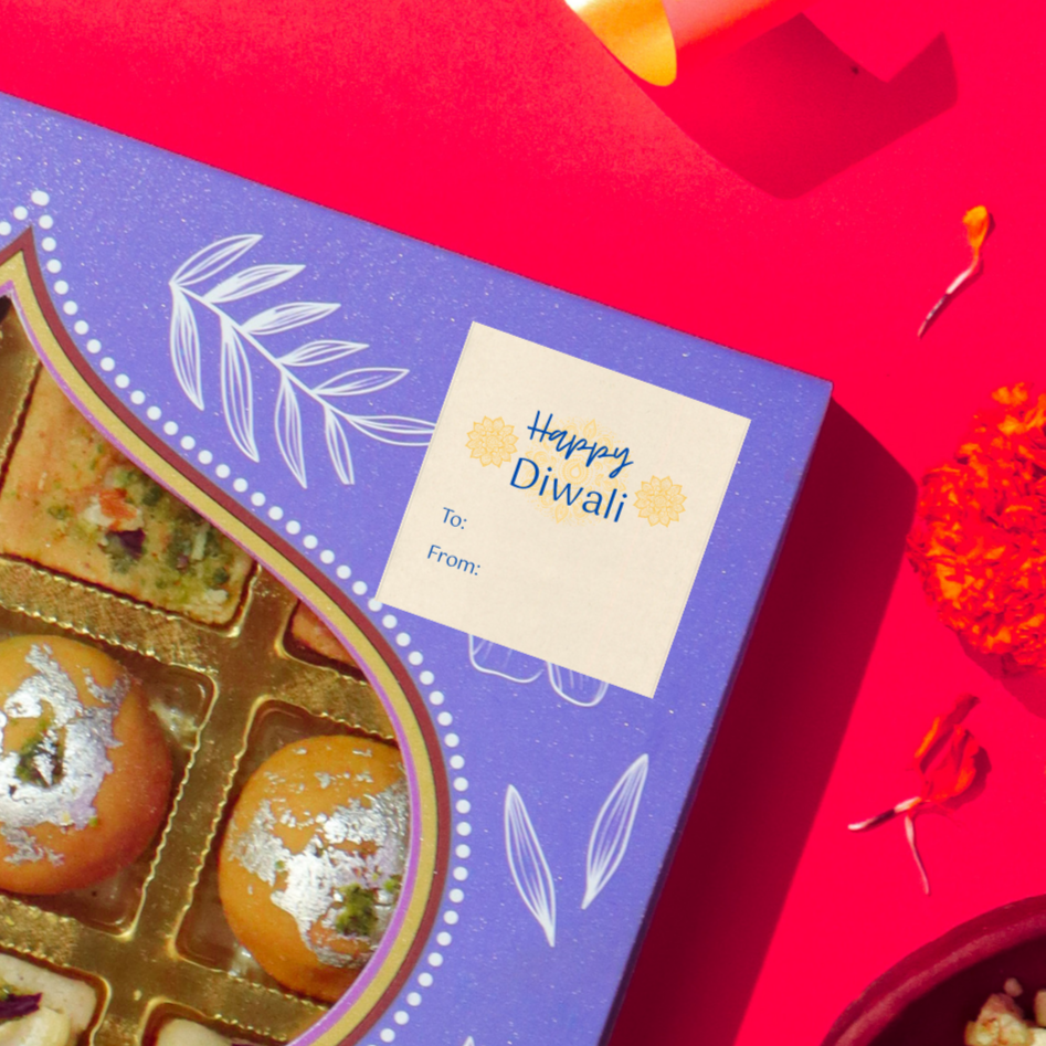 Diwali gift sticker, square, made from compostable sugarcane, with 'Happy Diwali' text and mandalas illustration. The sticker label is placed on a gift box of Diwali sweets on a red background