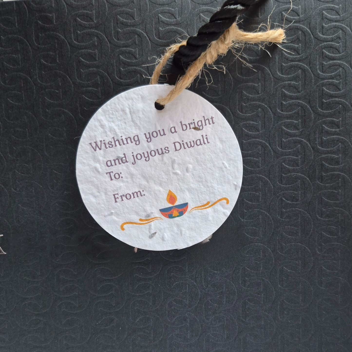 Round Diwali gift tag, made of seed paper, with 'wishing you a bright joyous Diwali' text and Diya illustration hanging from a black bag