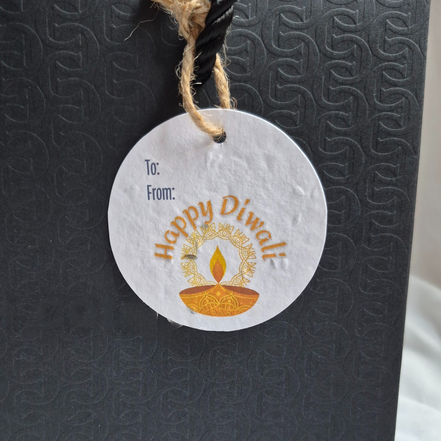 Round Diwali gift tag, made of seed paper, with 'Happy Diwali' text and diya illustration hanging from a black bag