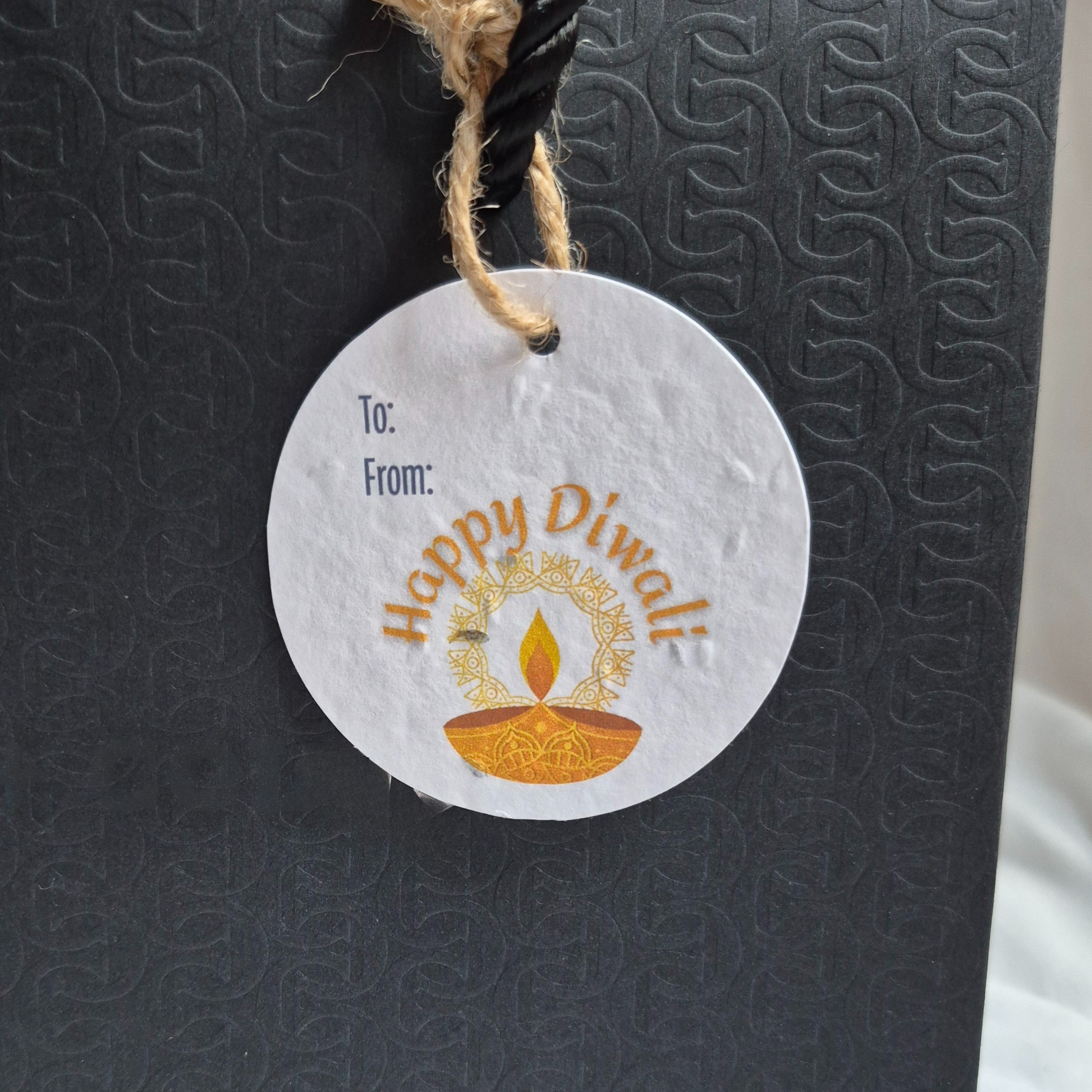 Round Diwali gift tag, made of seed paper, with 'Happy Diwali' text and diya illustration hanging from a black bag