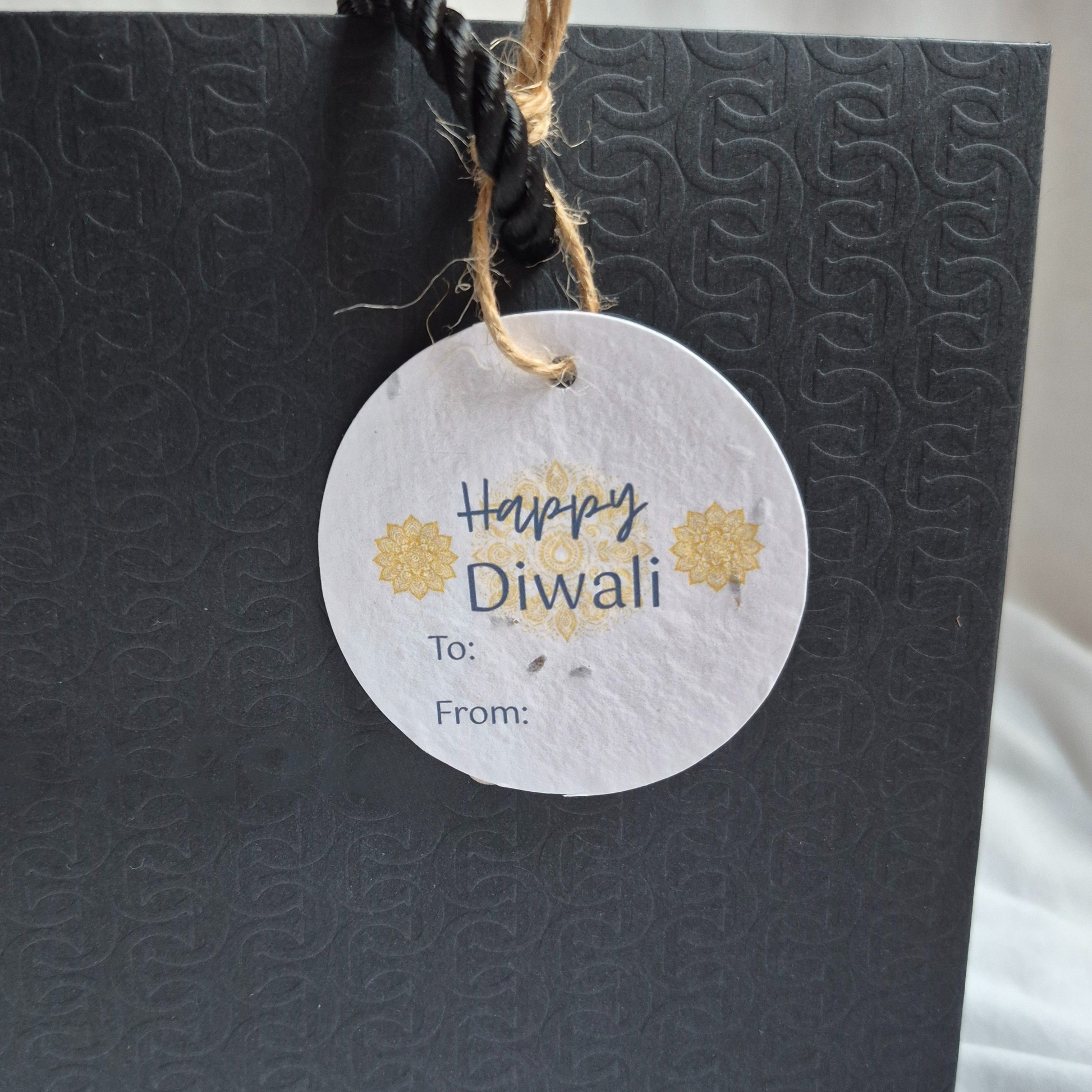 Round Diwali gift tag, made of seed paper, with 'Happy Diwali' text and mandalas illustration hanging from a black bag
