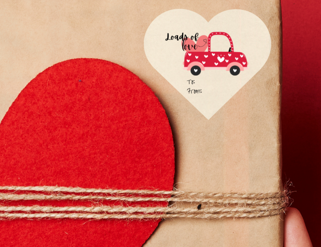 Heart shaped Gift sticker label for Valentine's day, with a red truck with a truckload filled with 'loads of love' text. The heart shaped sticker label is placed on a Gift box with red heart design held against a red background
