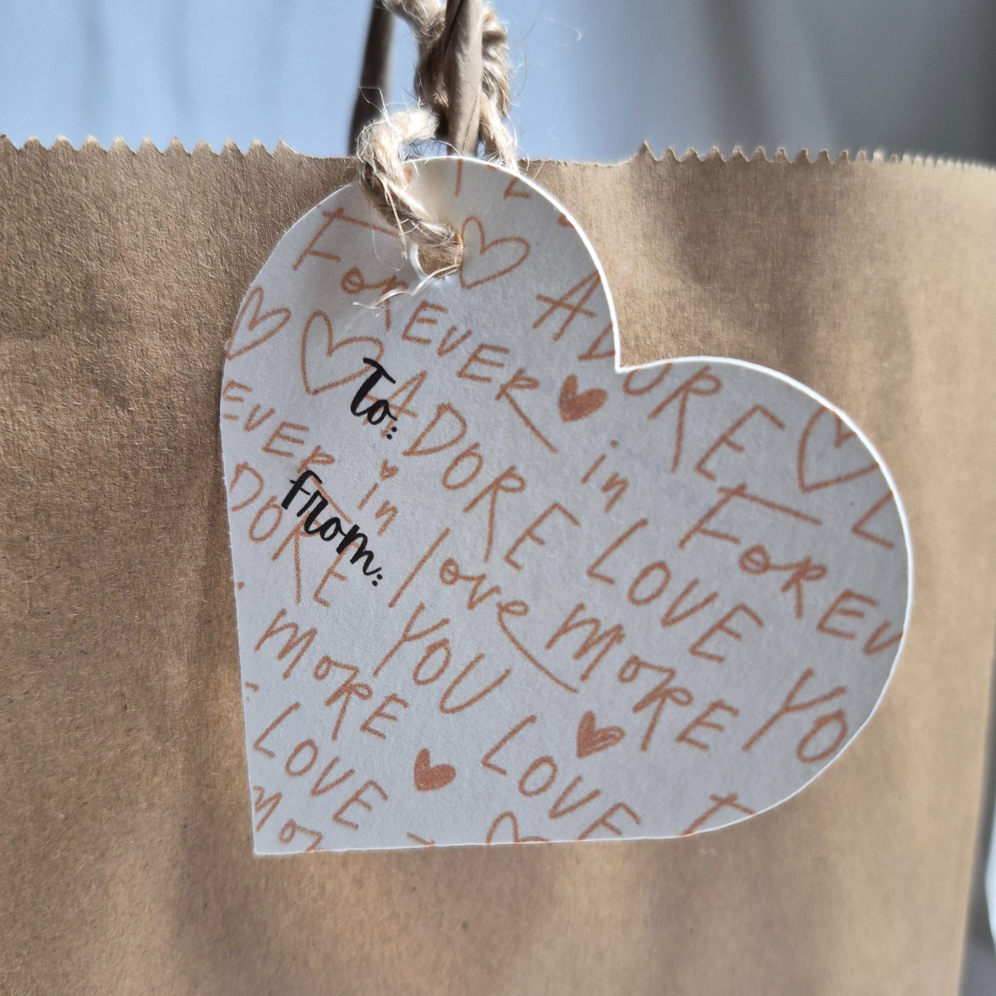 Heart-shaped  recycled paper gift tag with romantic text designs on a brown paper bag. Valentine's Day theme
