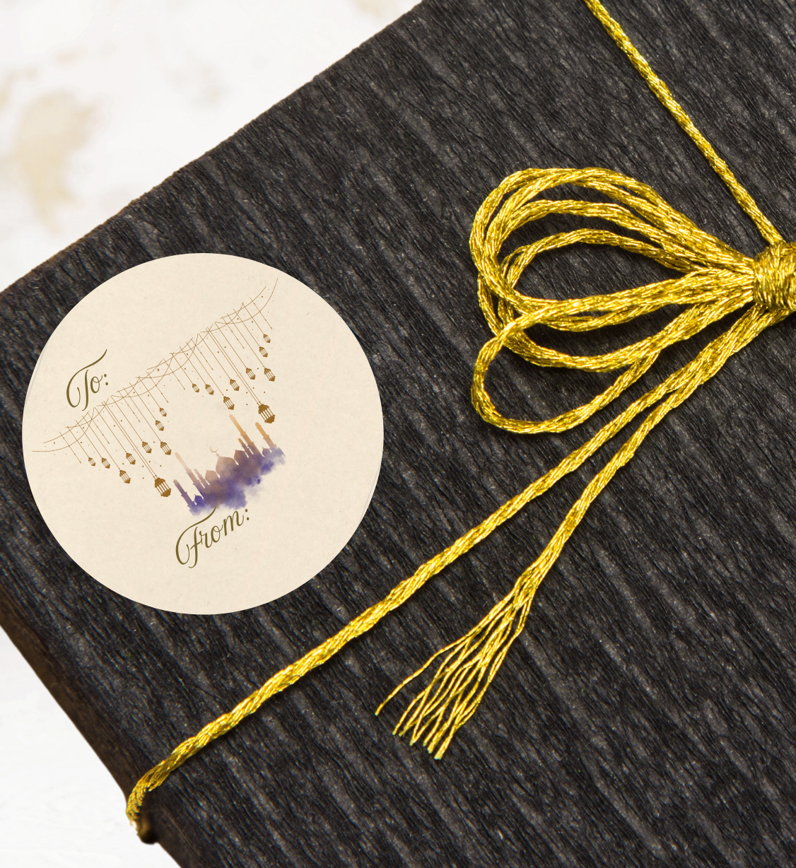 Black box with a gold string tied around it and a decorative gift label with a mosque and lanterns in gold purple and blue on a light background