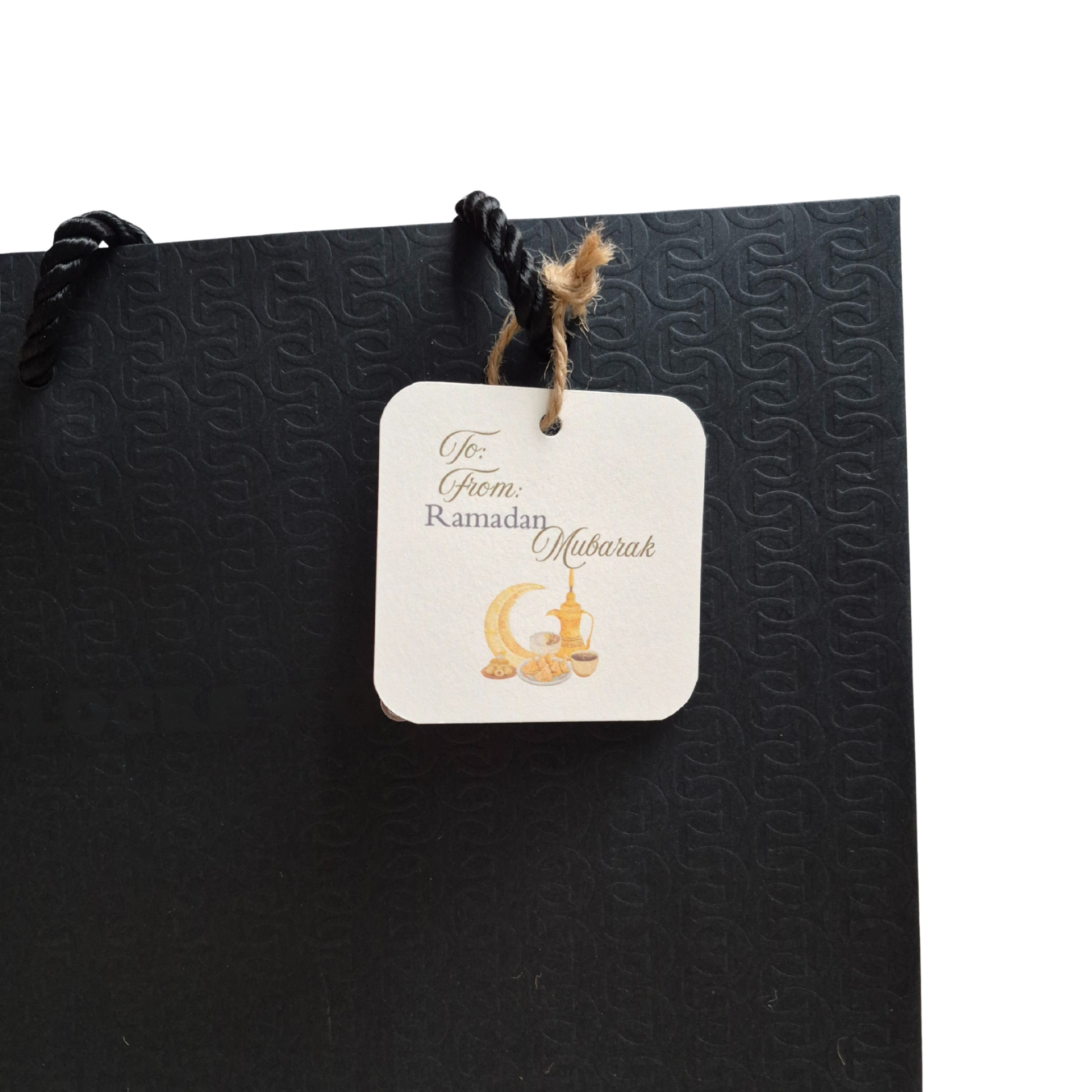 Ramadan recycled paper gift tag featuring 'Ramadan Mubarak' text and gold design. Hanging from a black gift bag.
