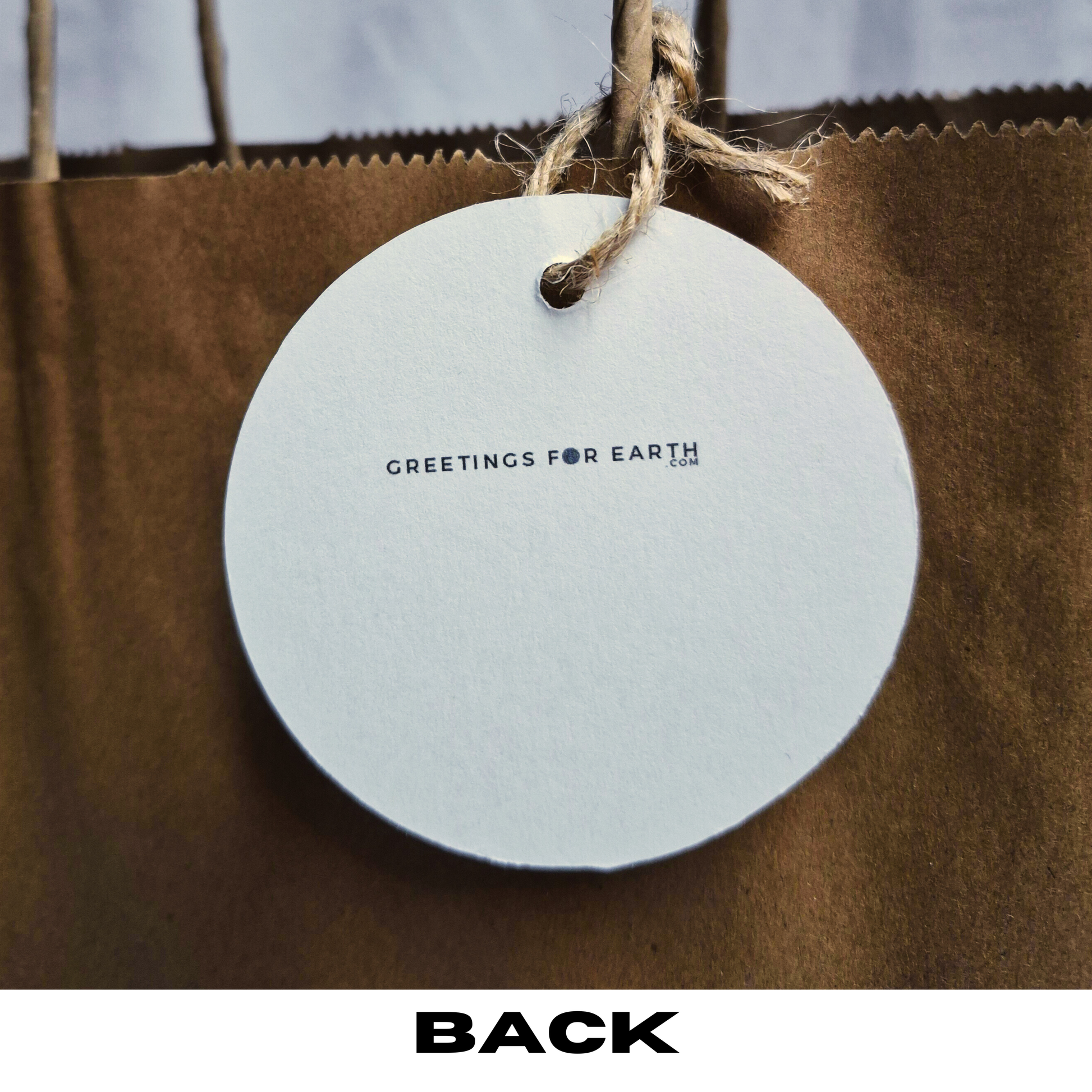 Rear of round recycled paper gift tag with 'Greetings for Earth.com' text on a brown paper bag.