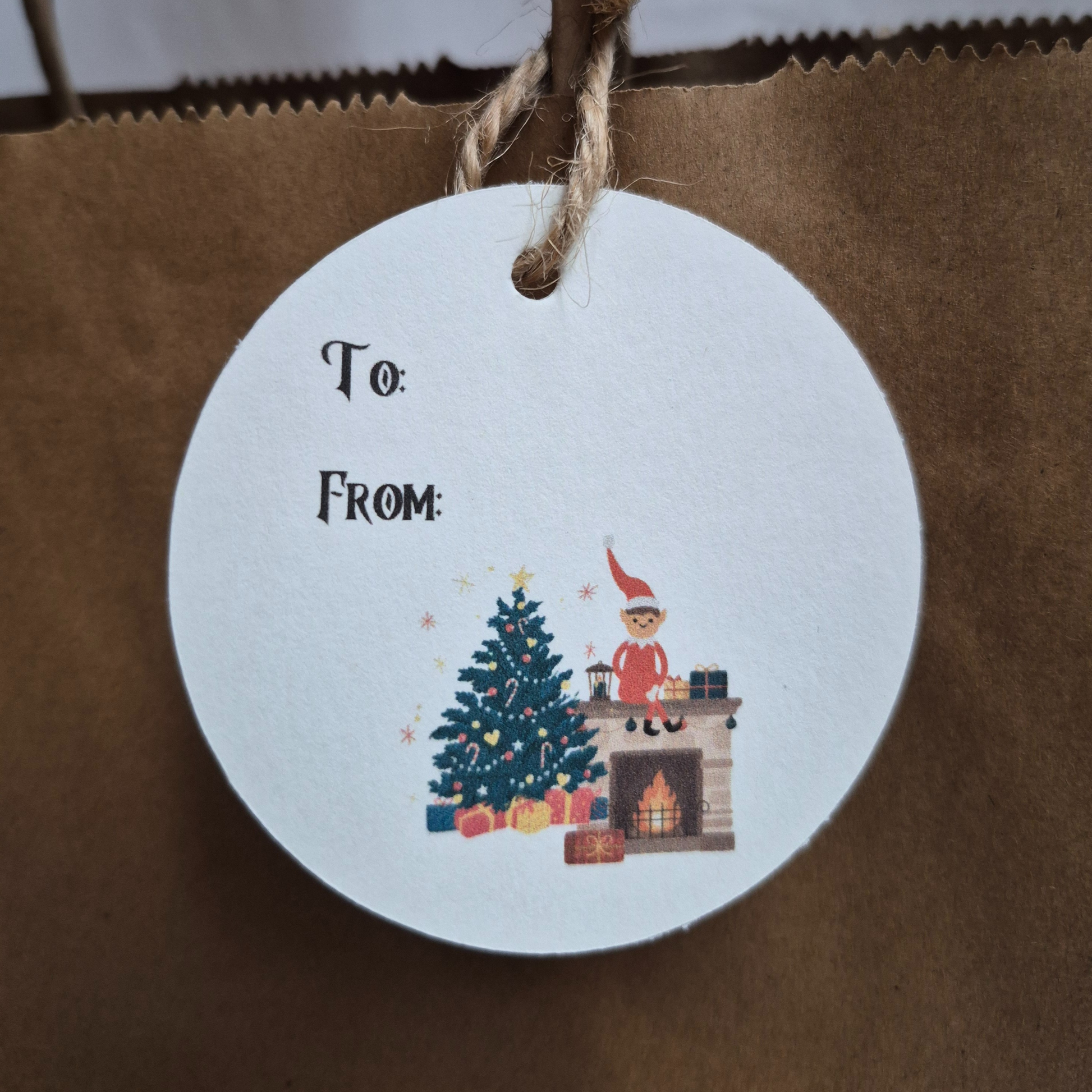 Round Recycled paper gift tag with Christmas decor and elf on the shelf hanging from a brown paper bag 