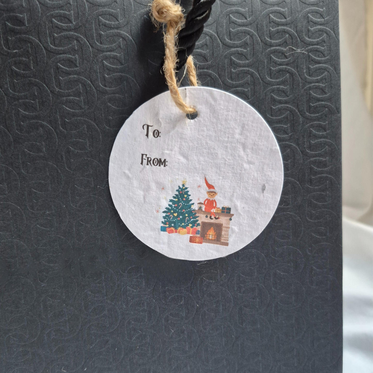 Round Christmas gift tag made of seed paper with Christmas decor and an elf on the shelf hanging from a black bag