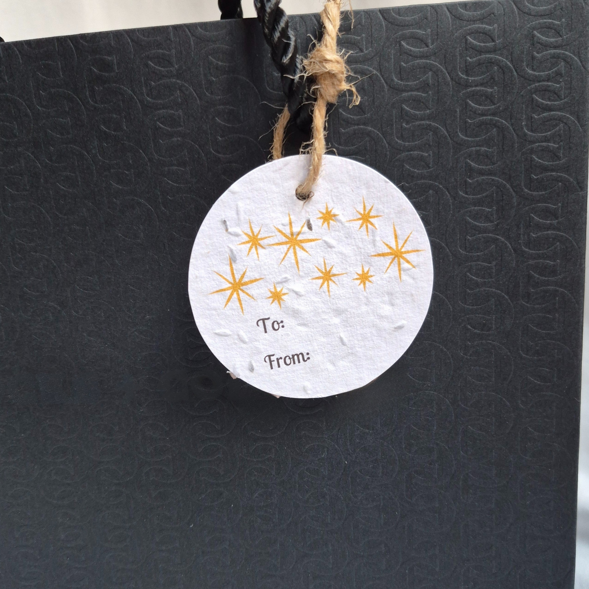 Round Christmas gift tag made of seed with gold stars hanging from a hanging from a black bag