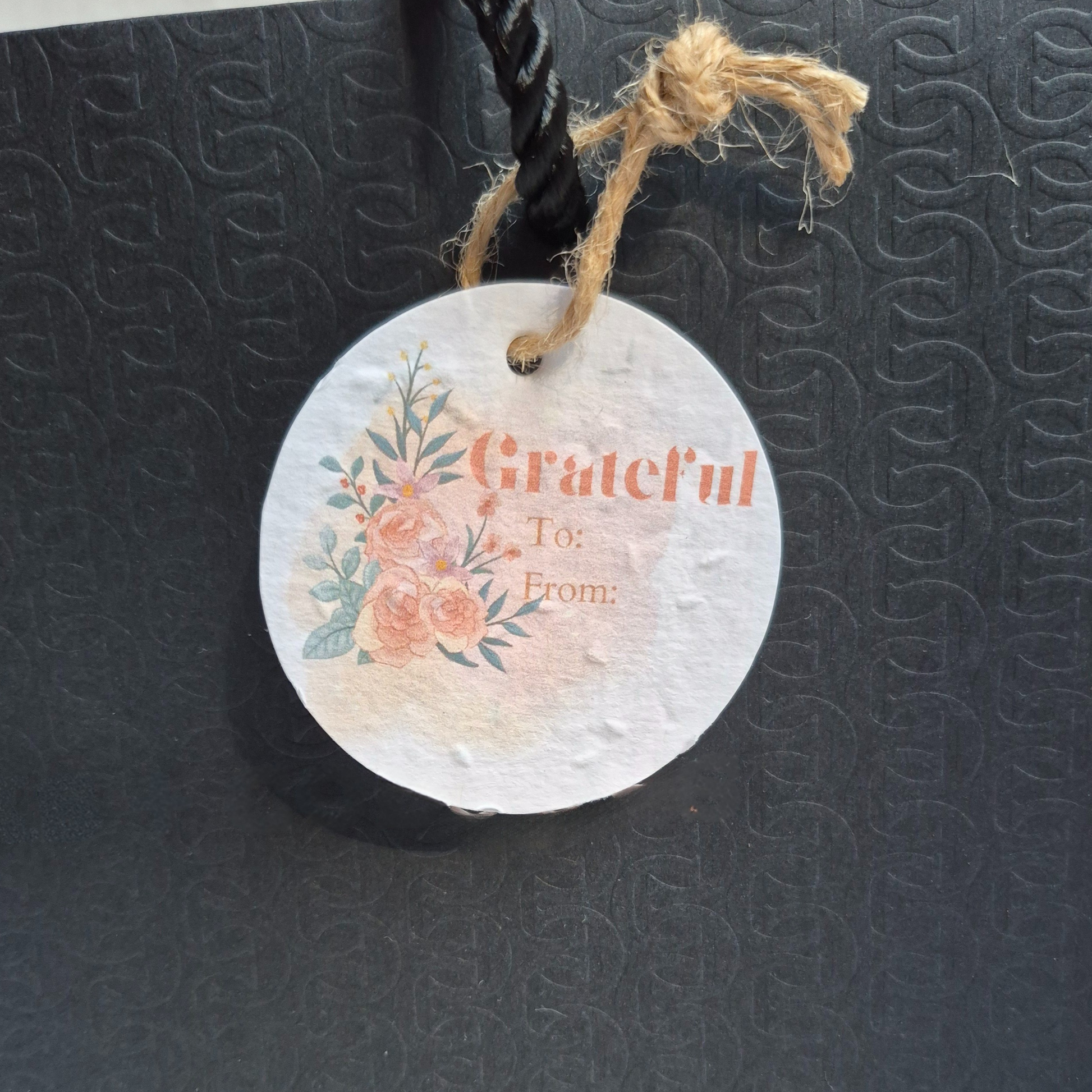 Round Thank you gift tag made of seed paper with floral design and 'Grateful To: From:' text on a brown paper bag.