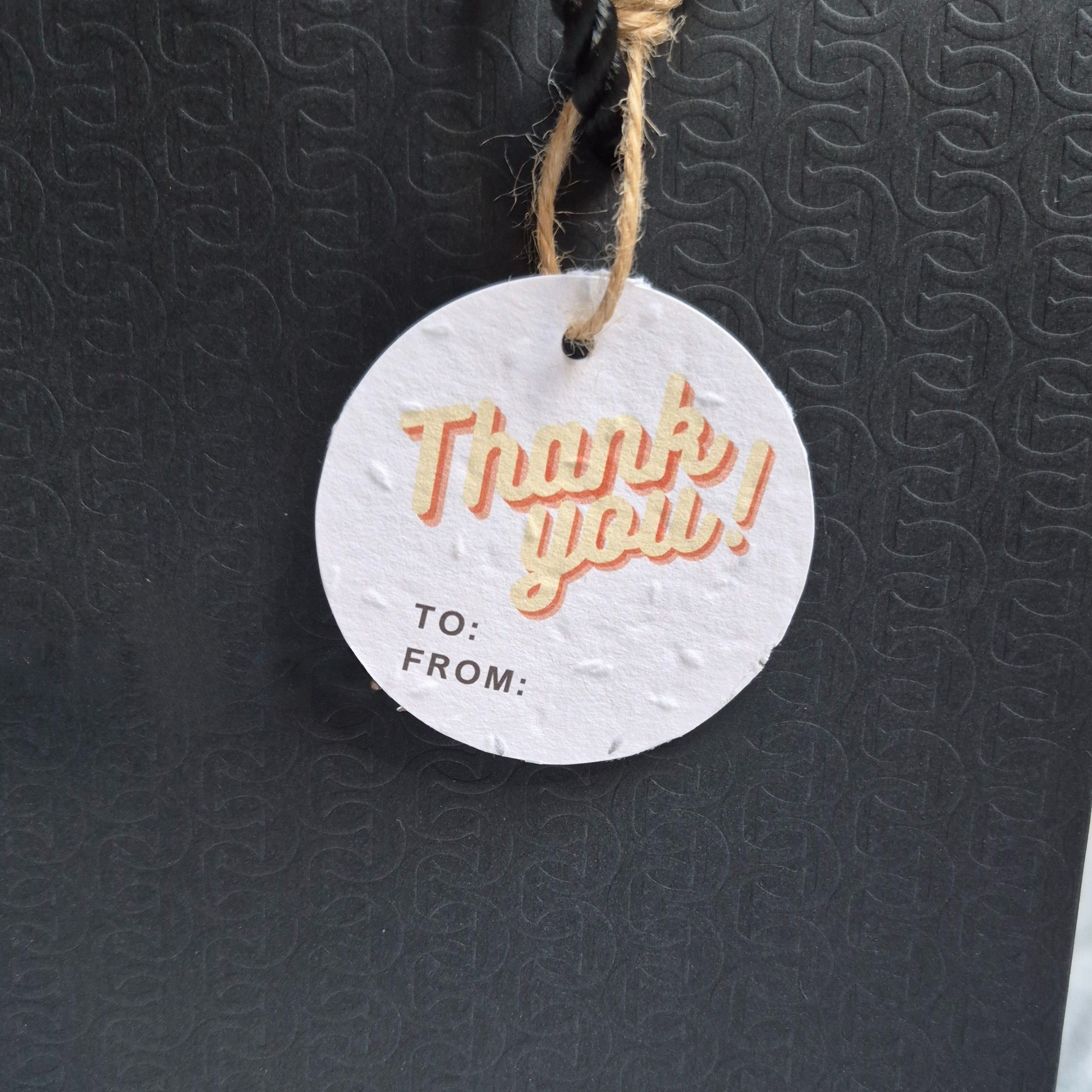 Round seed paper tag with 'Thank you!' text in a retro design on a textured black background