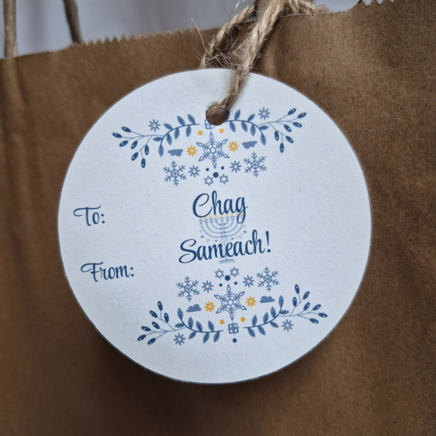 Round Hanukkah gift tag with 'Chag Sameach!' text on a brown paper bag