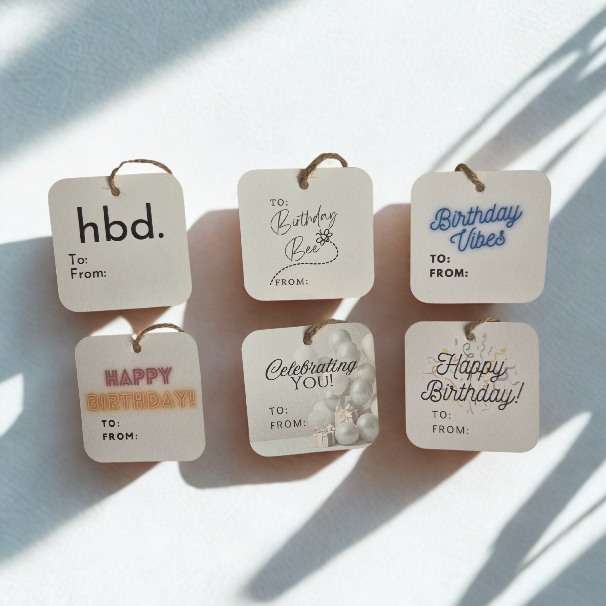 Set of six square birthday gift tags made of recycled paper with various messages on a light background