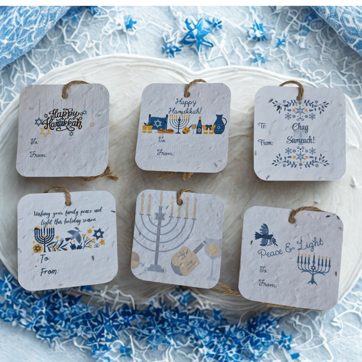 Set of  six Hanukkah-themed gift tags made of seed paper, on a decorative plate with blue and white floral pattern.
