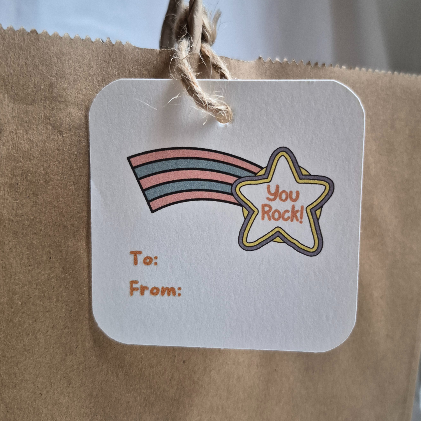 Square congratulations gift tag made with recycled paper with rainbow and star with 'you rock' design on a brown paper bag