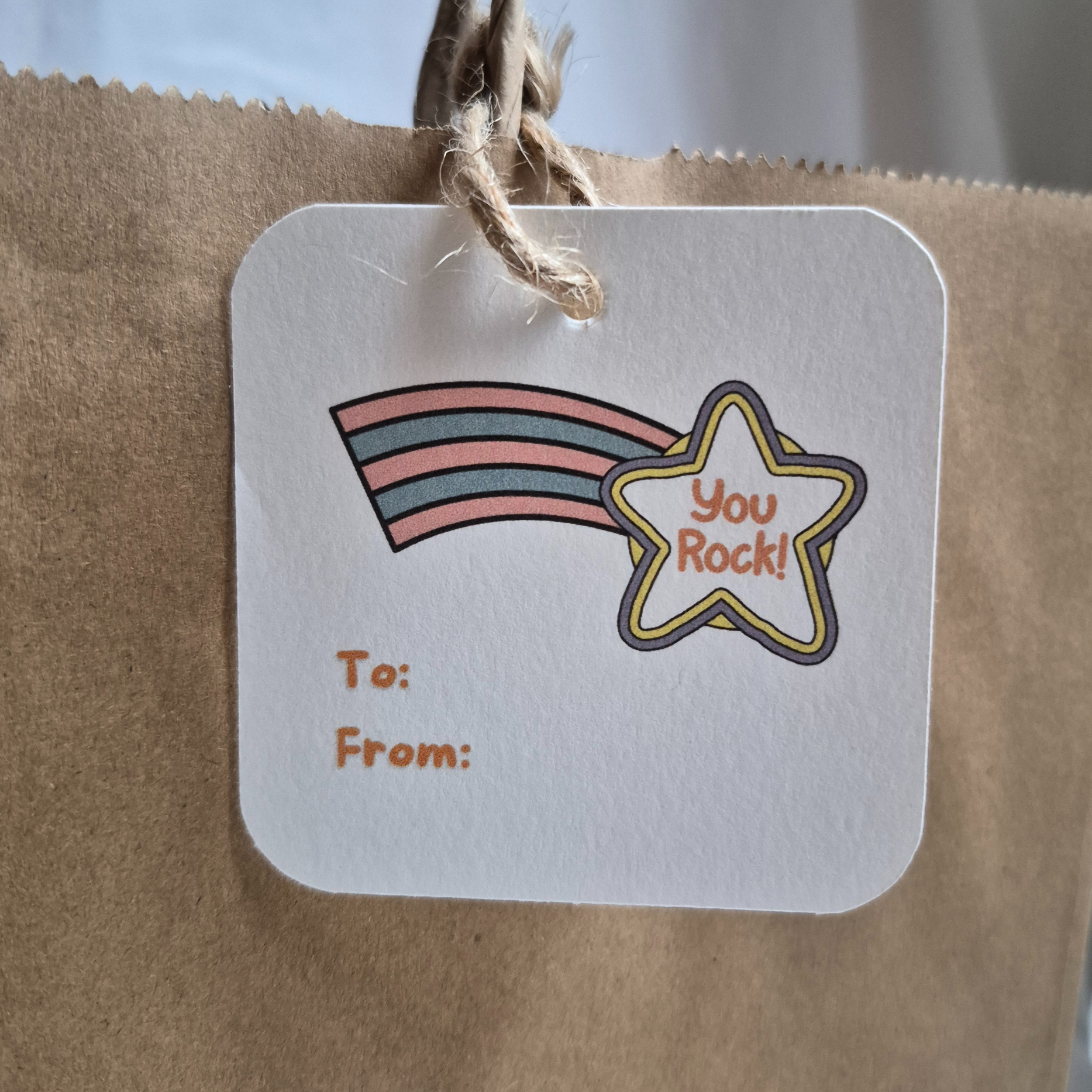 Square congratulations gift tag made with recycled paper with rainbow and star with 'you rock' design on a brown paper bag